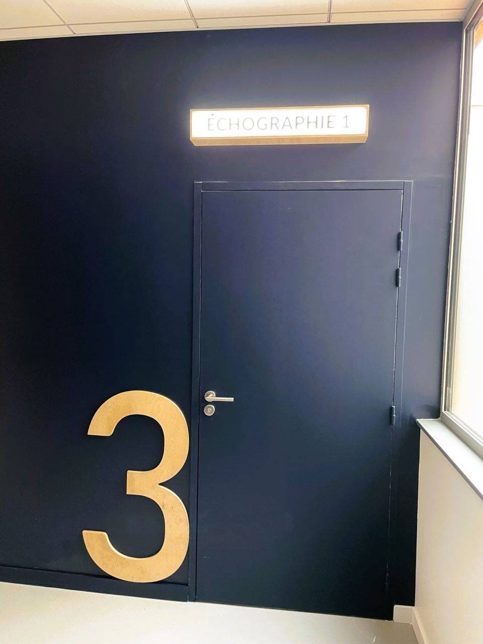 La porte bleu nuit de la salle d’échographie et son chiffre en bois