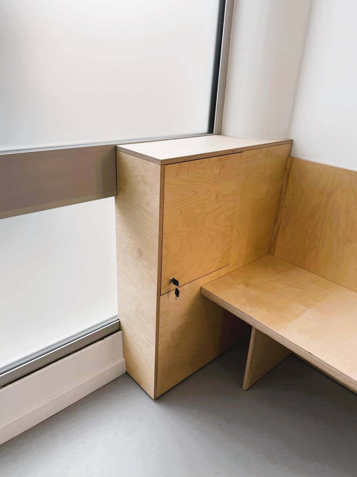 Le bout de banquette en contreplaqué et son casier, devant la fenêtre